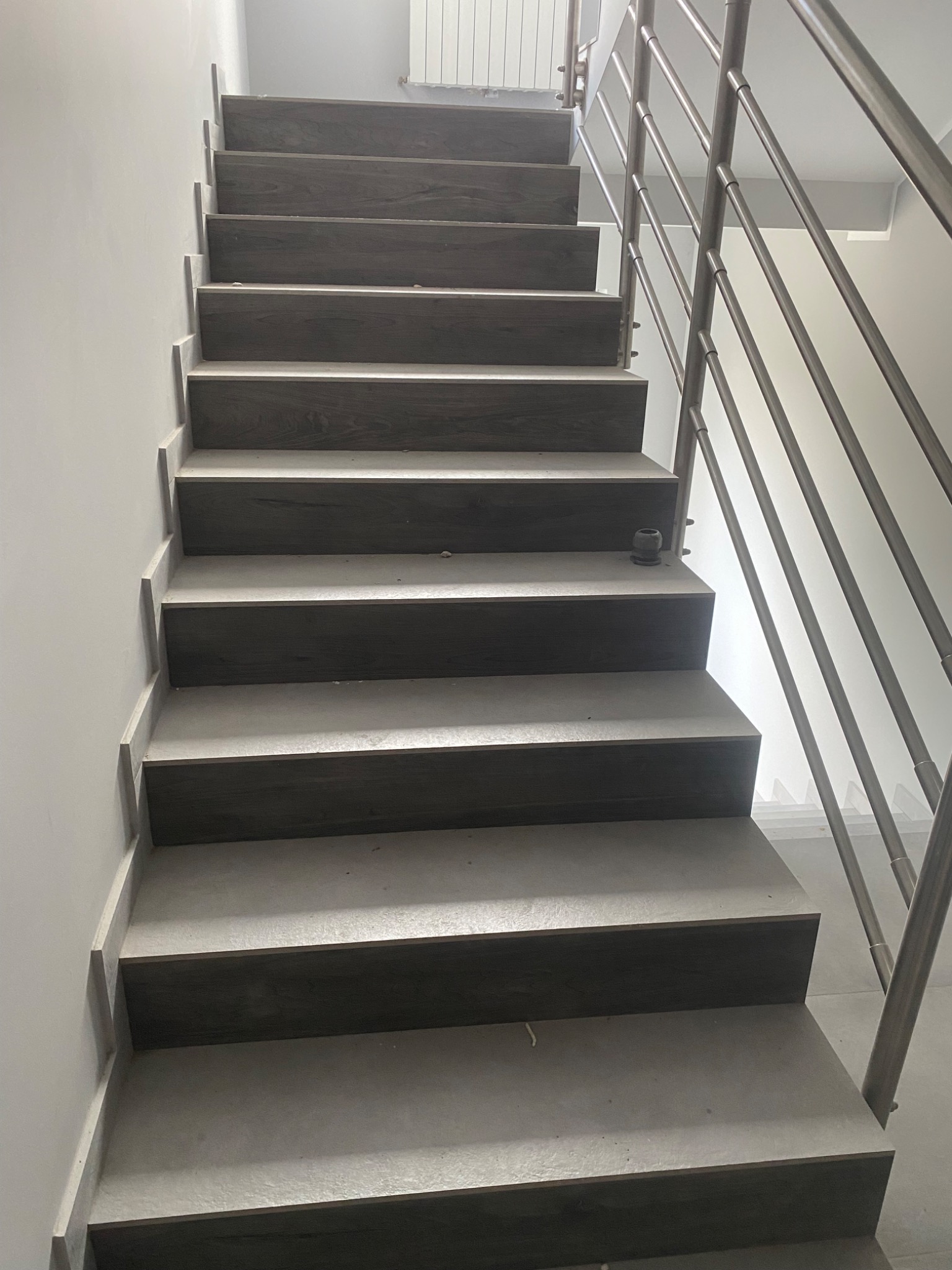 Schody wewnętrzne z drewnopodobnymi stopniami i metalową balustradą, widok z dołu, jasne wnętrze.