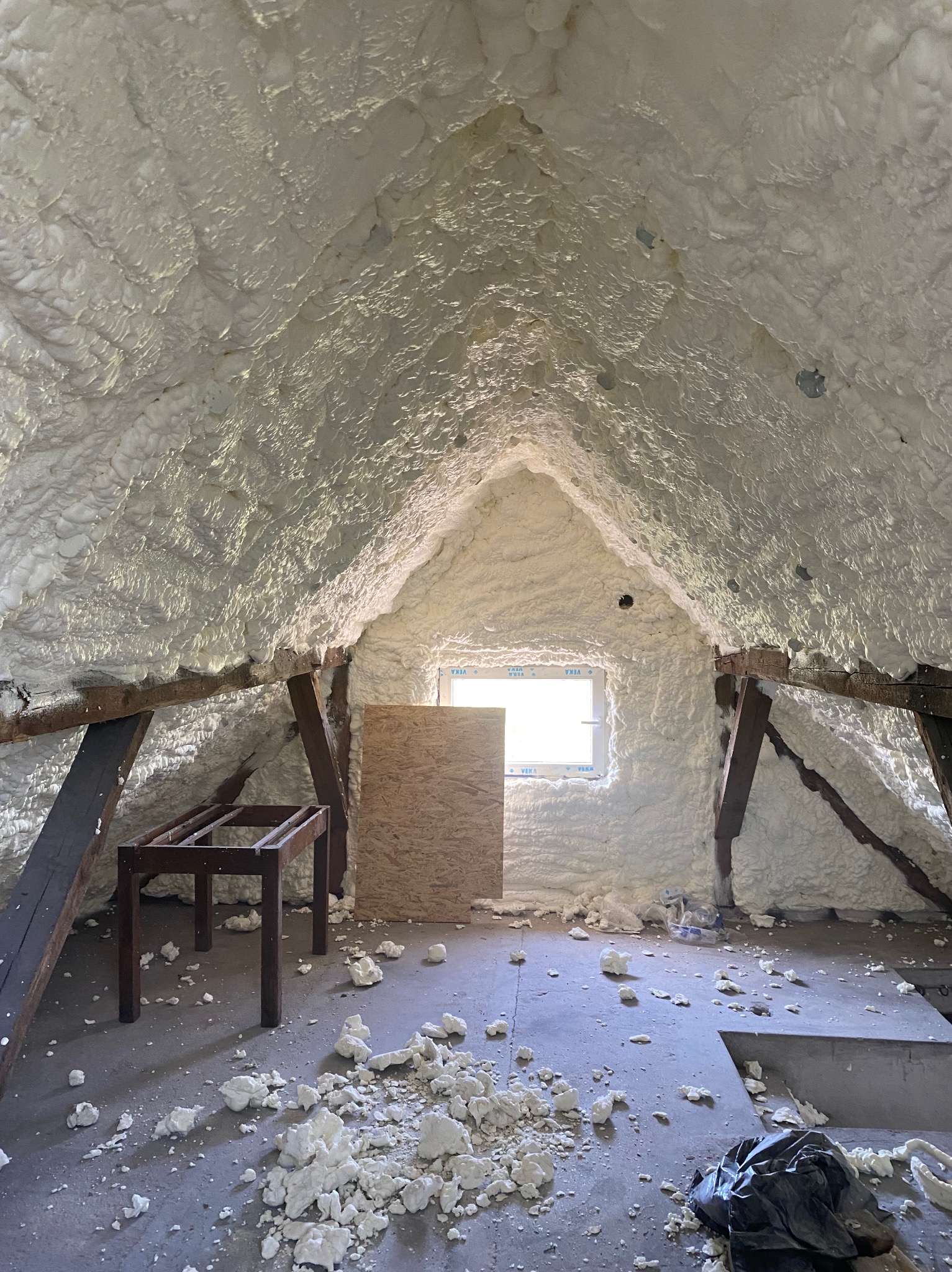 Poddasze po ociepleniu pianką PUR, widoczne drewniane elementy konstrukcyjne i okno. Na podłodze resztki piany.