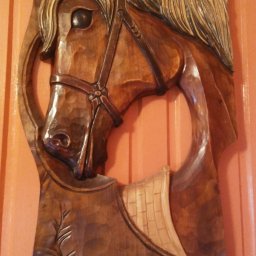 Klimkówka - Ręcznie rzeźbiona w drewnie płaskorzeźba przedstawiająca głowę konia w uprzęży, z widocznymi detalami sierści i roślinnym motywem u dołu, zawieszona na ścianie z pionowymi panelami.