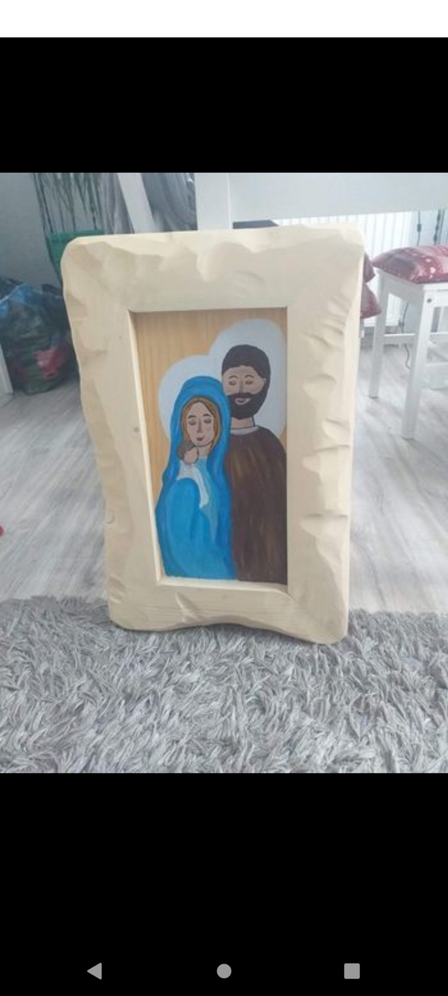 Ręcznie malowany obraz Świętej Rodziny w drewnianej ramie o nieregularnych krawędziach, ustawiony na szarym dywanie.