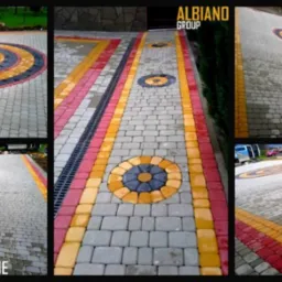 Kolorowa kostka brukowa ułożona w geometryczne wzory, z centralnym okrągłym motywem i drenażem liniowym. Prezentacja realizacji firmy brukarskiej.