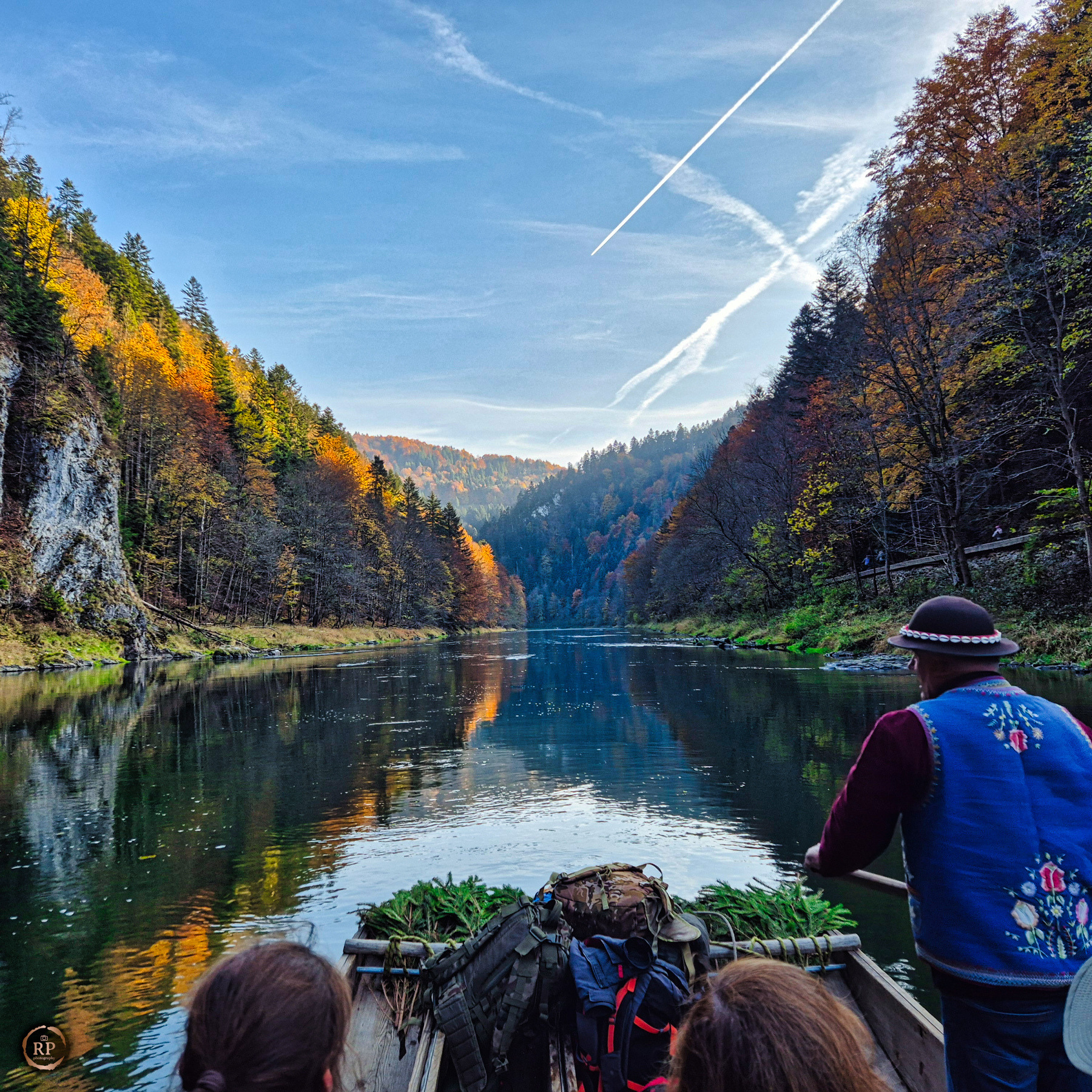 Spływ Dunajcem w jesiennej scenerii. Flisak w tradycyjnym stroju steruje łodzią, widok z perspektywy pasażera na malowniczy krajobraz Pienin.