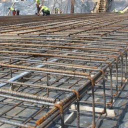 Siatka zbrojeniowa z pręt&oacute;w stalowych, tworząca szkielet konstrukcji, z widocznymi pracownikami w tle, przygotowywana do zalania betonem.