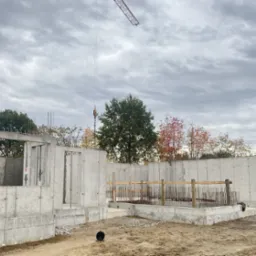 Stan surowy zamknięty budynku żelbetowego w Tarnowie, widok na fundamenty i ściany z betonu, zbrojenia oraz żuraw na tle pochmurnego nieba.