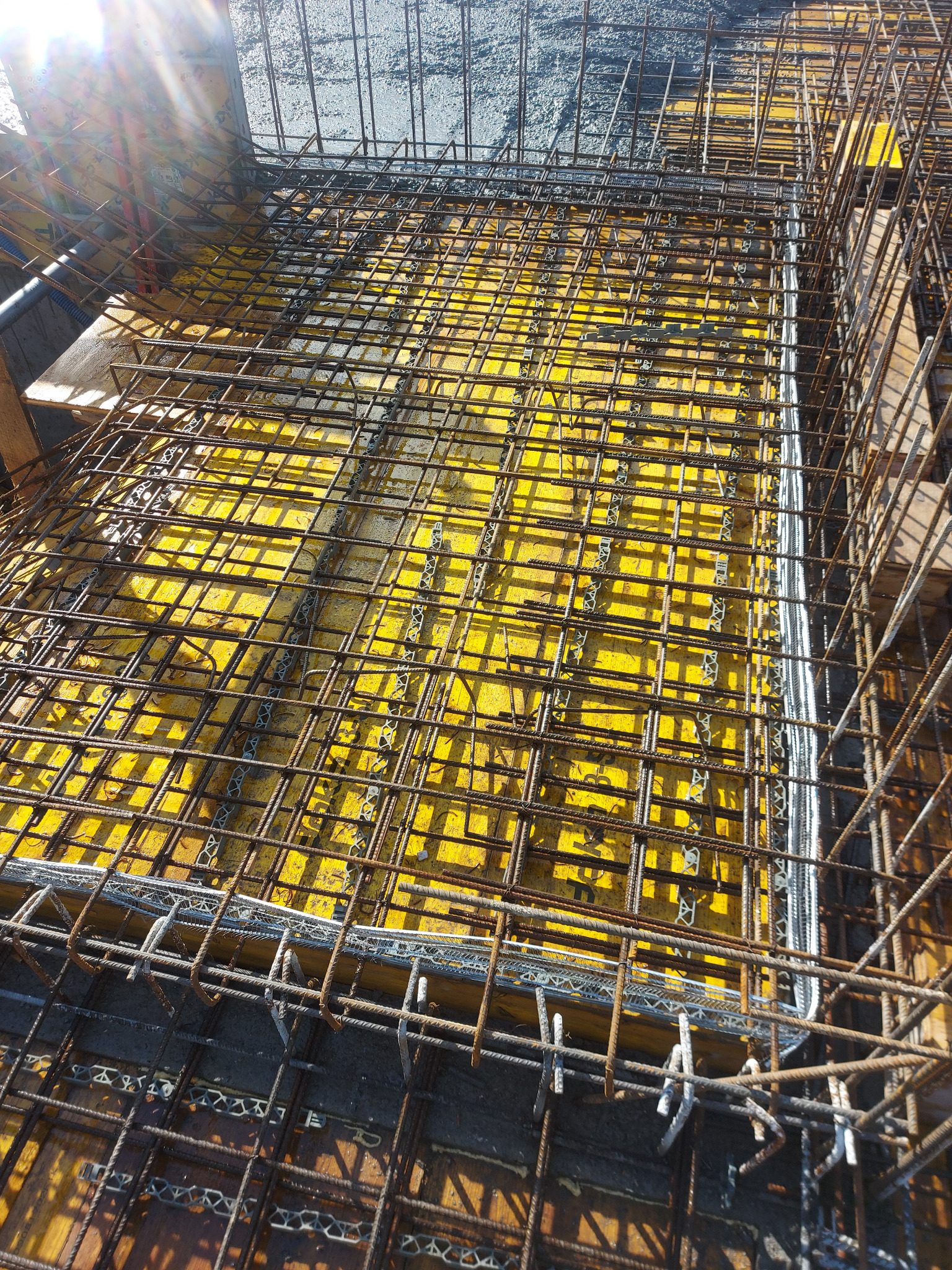 Siatka zbrojeniowa ułożona na żółtym szalunku, widok z góry na przygotowany fundament pod budynek.