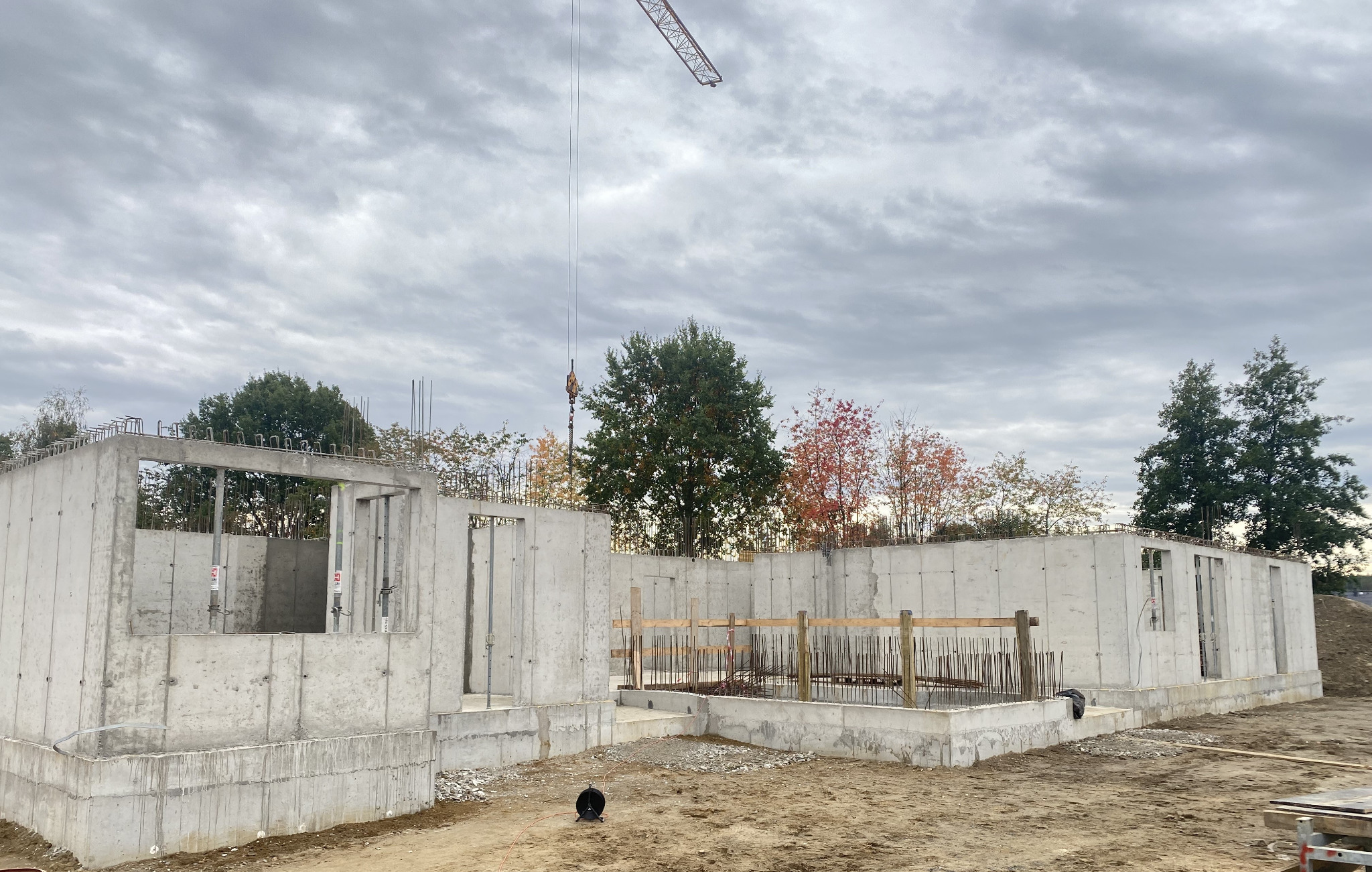 Stan surowy zamknięty budynku żelbetowego w Tarnowie, widok na fundamenty i ściany z betonu, zbrojenia oraz żuraw na tle pochmurnego nieba.