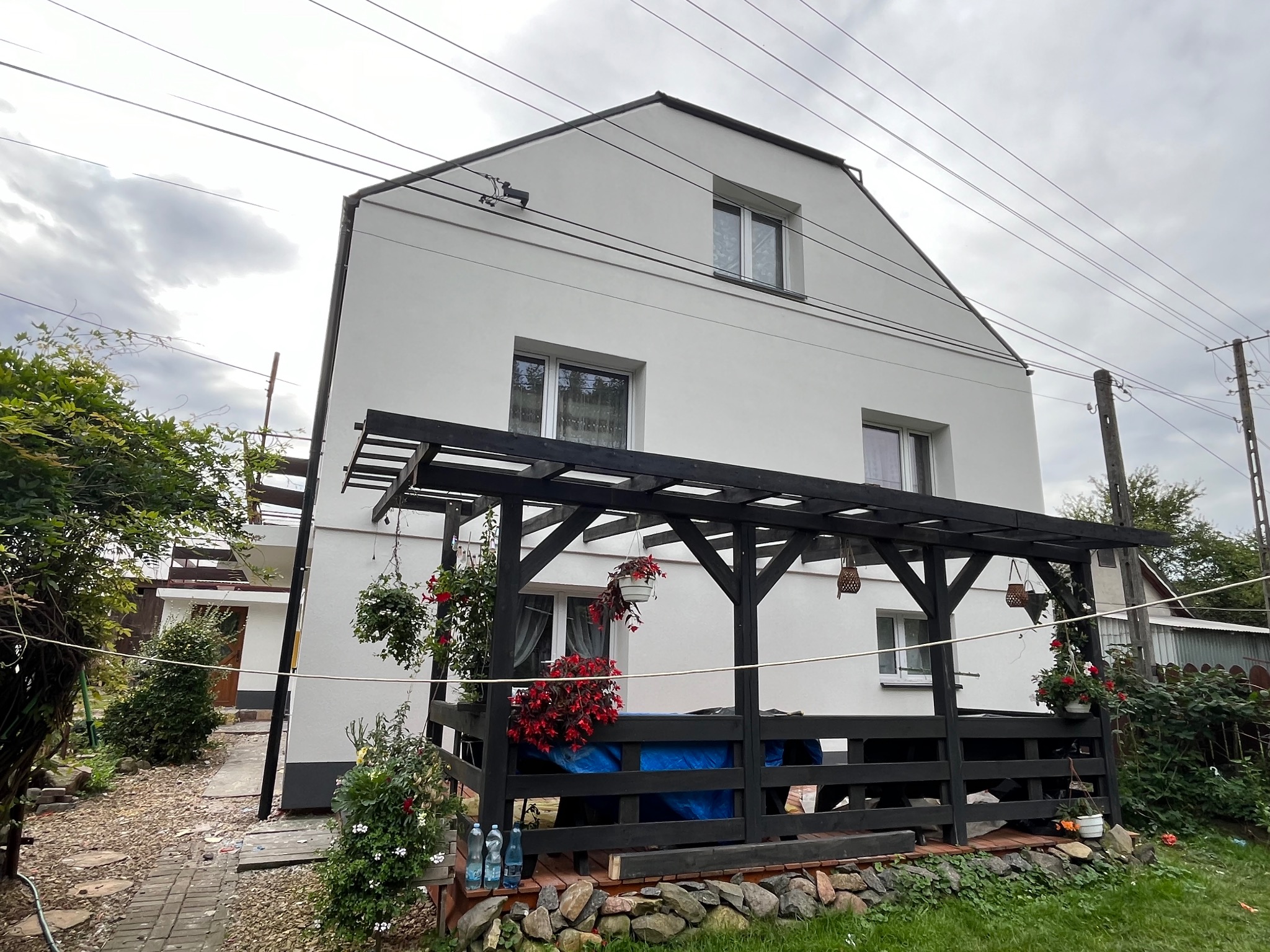 Dom jednorodzinny po renowacji elewacji w Wielopolu Skrzyńskim, widok z ogrodu na jasną fasadę i drewnianą pergolę z kwiatami.