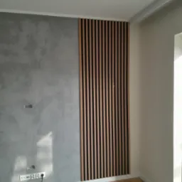 Nowoczesna ściana z dekoracyjną gładzią i drewnianymi lamelami w pionowym układzie, uzupełniona o listwę przypodłogową i parkiet w jodełkę.