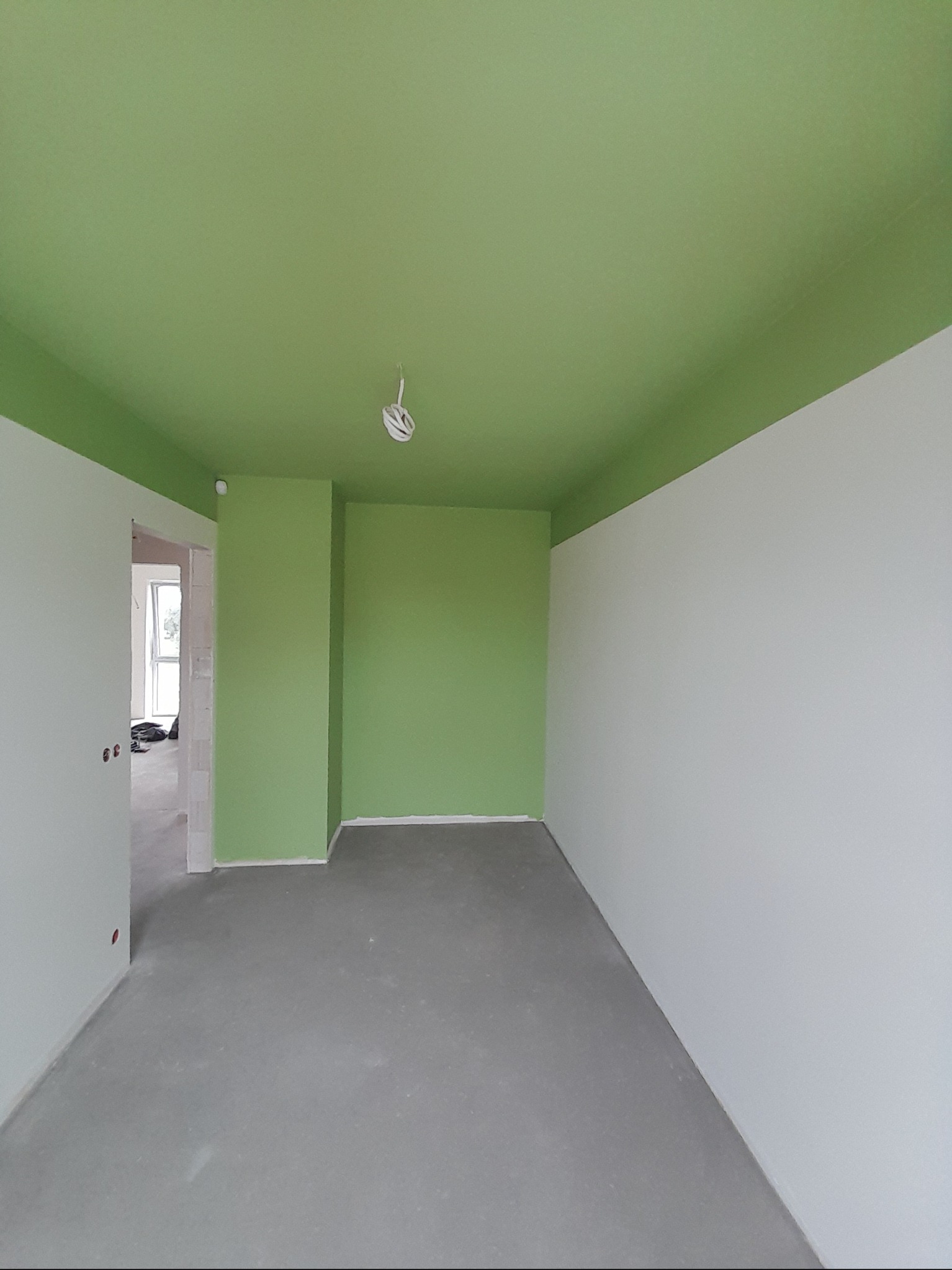 Pokój po malowaniu: zielony sufit i górna część ścian, dolna część ścian biała. Szara podłoga. Widoczne niedoskonałości wykończenia.