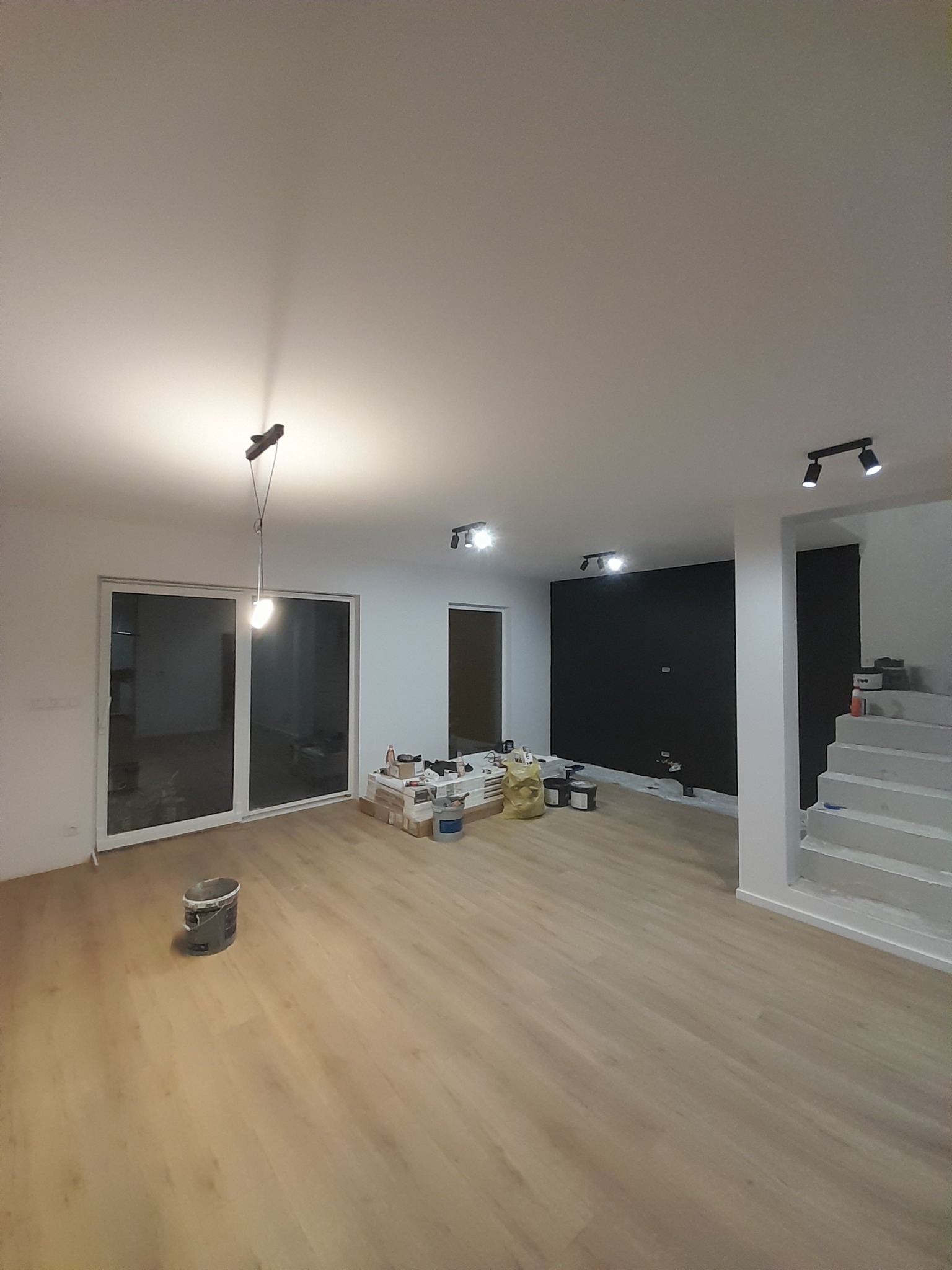 Wnętrze w trakcie odświeżania w Poznaniu: panele podłogowe, ściana pomalowana na czarno, widoczne puszki z farbą i akcesoria malarskie, schody w stanie surowym.