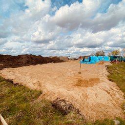 M&M Płyty Sp. Z o.o. - Przygotowany teren pod budowę z wykopanym piaskiem, widoczne materiały izolacyjne i firmowy bus w tle.