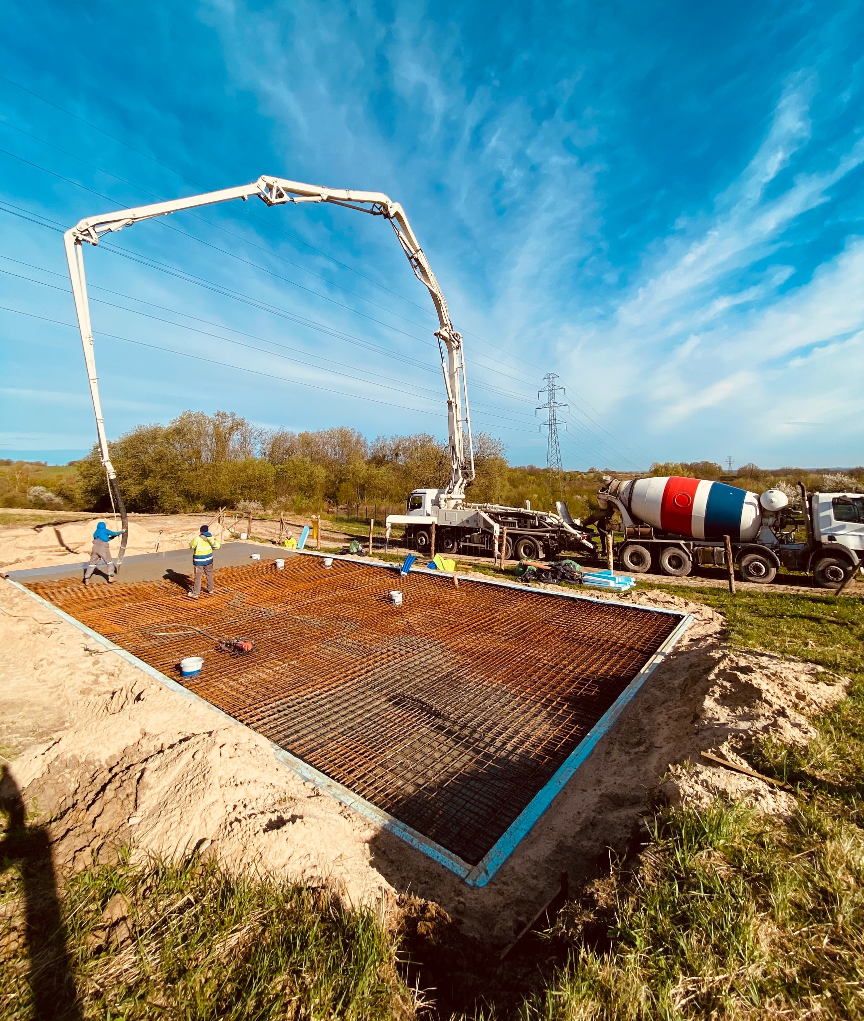Wylewanie betonu na zbrojenie fundamentu za pomocą pompy do betonu i betonomieszarki w słoneczny dzień.