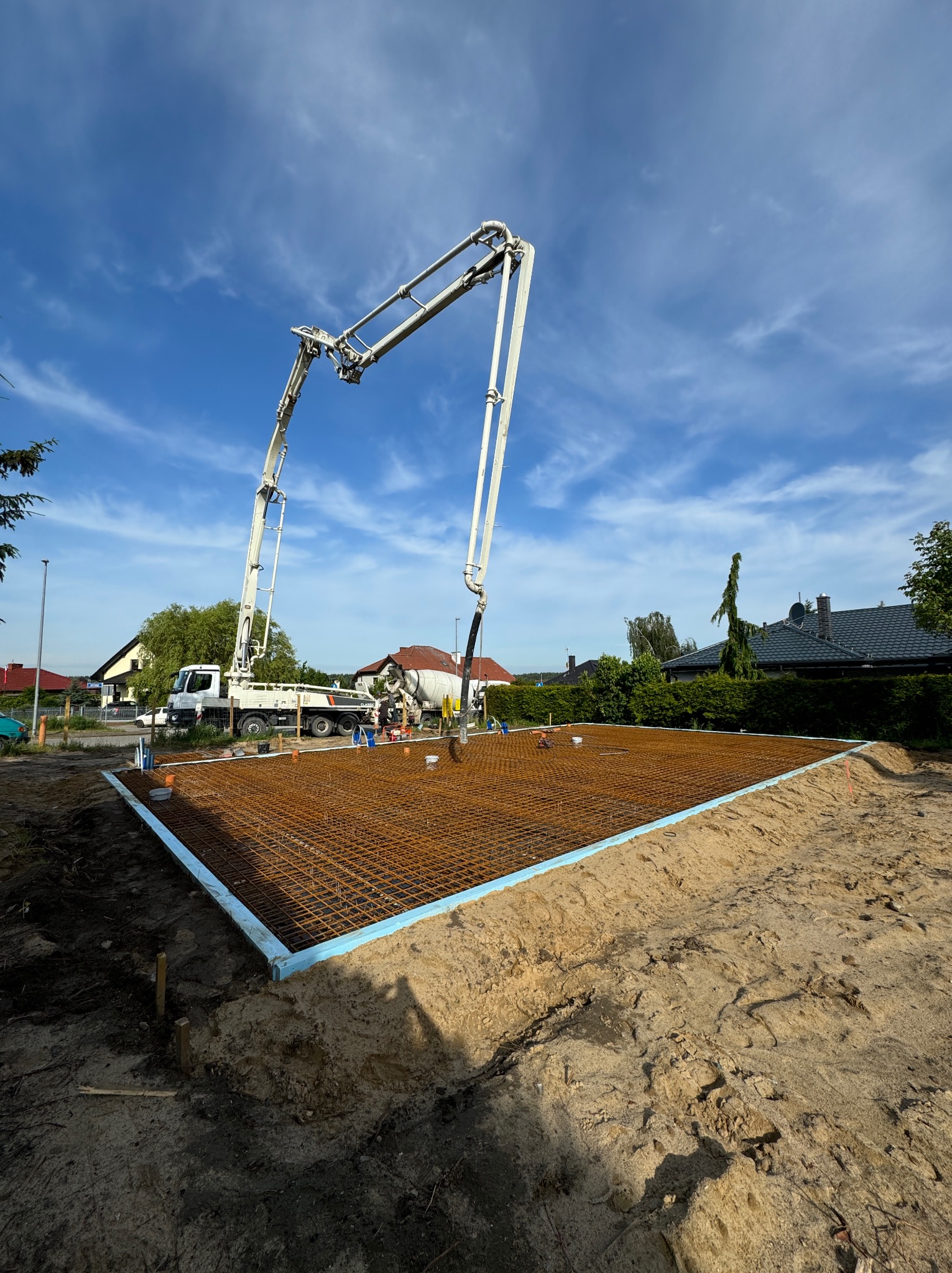 Wylewanie betonu na przygotowane zbrojenie fundamentu domu jednorodzinnego za pomocą pompy do betonu na tle błękitnego nieba.