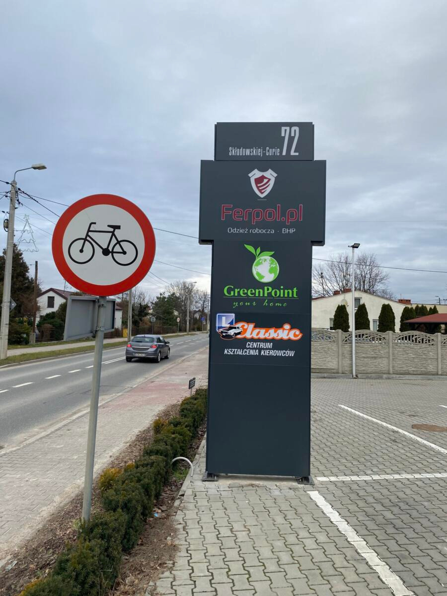 Tablica reklamowa z logo firm Ferpol.pl, GreenPoint i Classic Centrum Kształcenia Kierowców przy ulicy Skłodowskiej-Curie 72, obok znak zakazu ruchu rowerów.