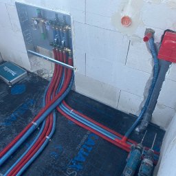 G TECH Kacper Olszewski - Rozprowadzenie rur instalacji grzewczej podłogowej w surowym stanie, widoczne rury czerwone i niebieskie, narzędzia i skrzynka narzędziowa Makita.