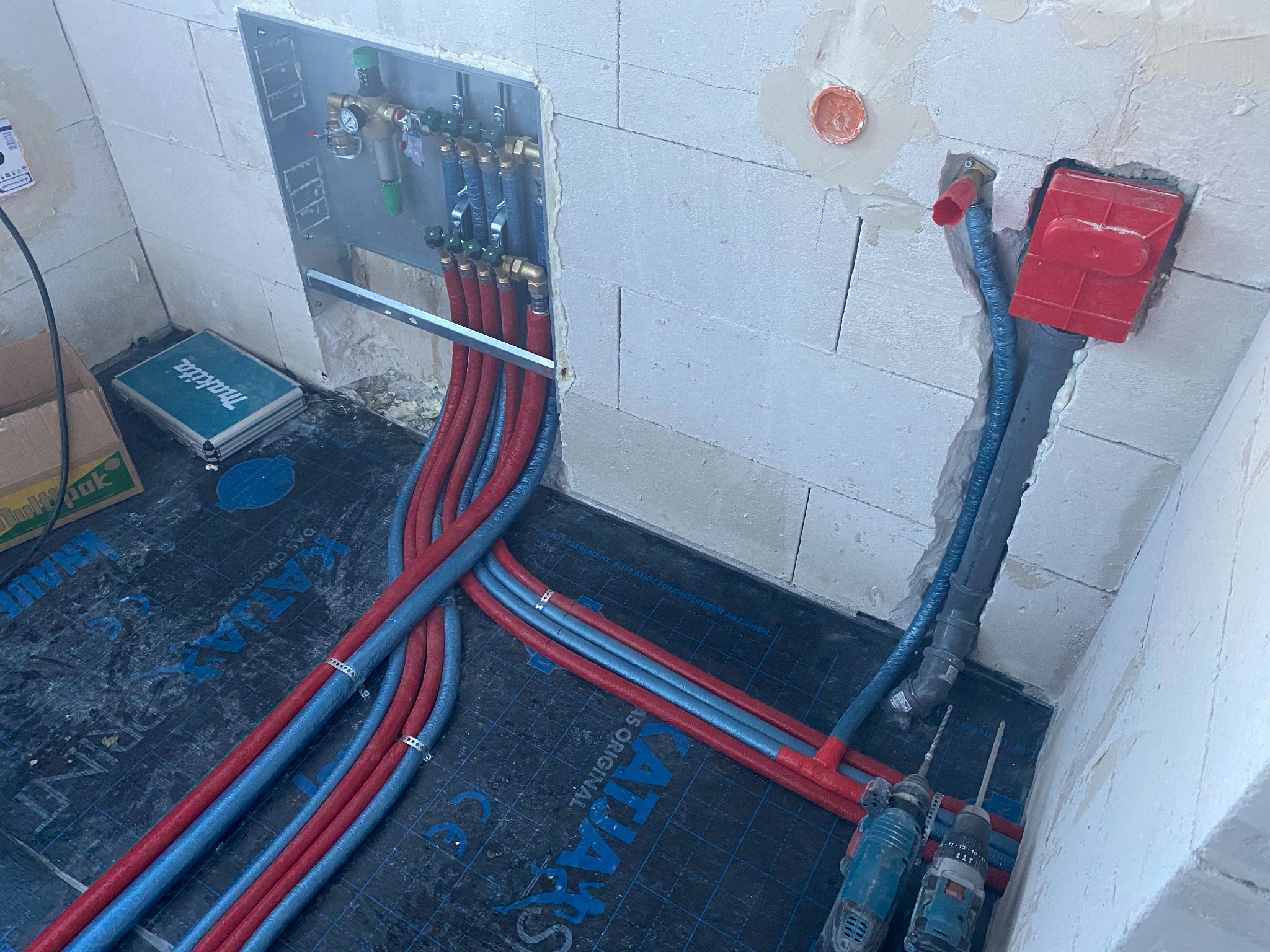 Rozprowadzenie rur instalacji grzewczej podłogowej w surowym stanie, widoczne rury czerwone i niebieskie, narzędzia i skrzynka narzędziowa Makita.