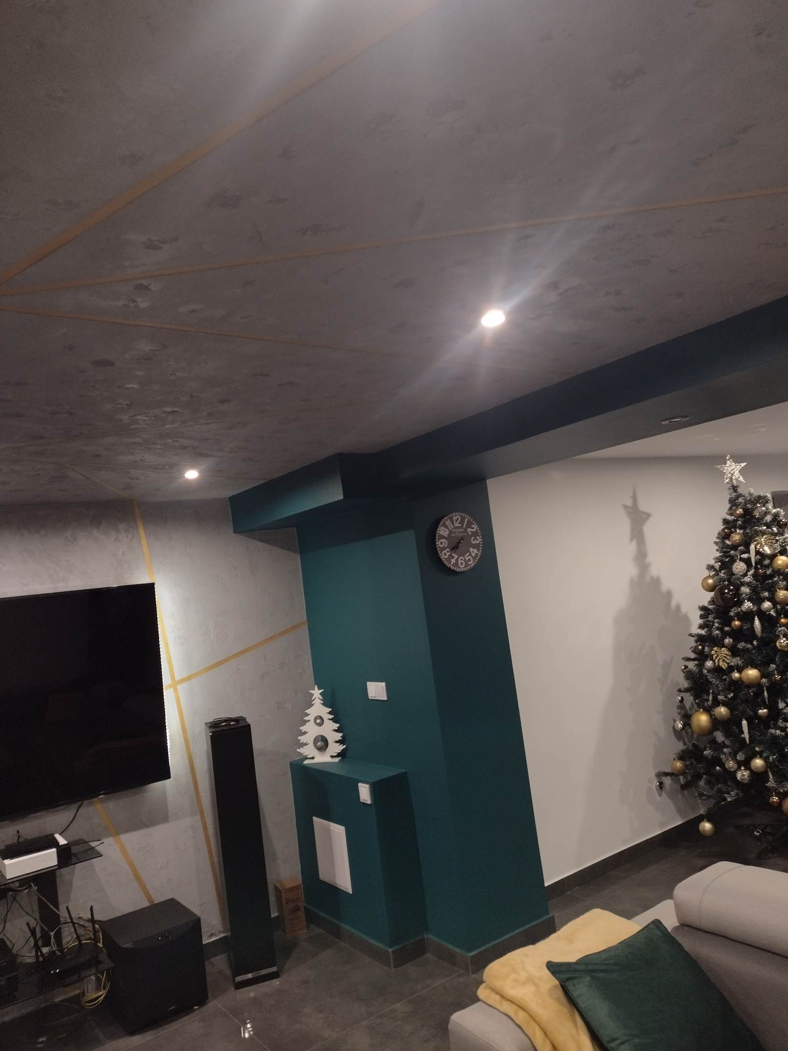 Pokój dzienny z dekoracyjnym tynkiem na suficie i ścianach, akcentem w postaci turkusowej kolumny, choinką i zegarem na ścianie.