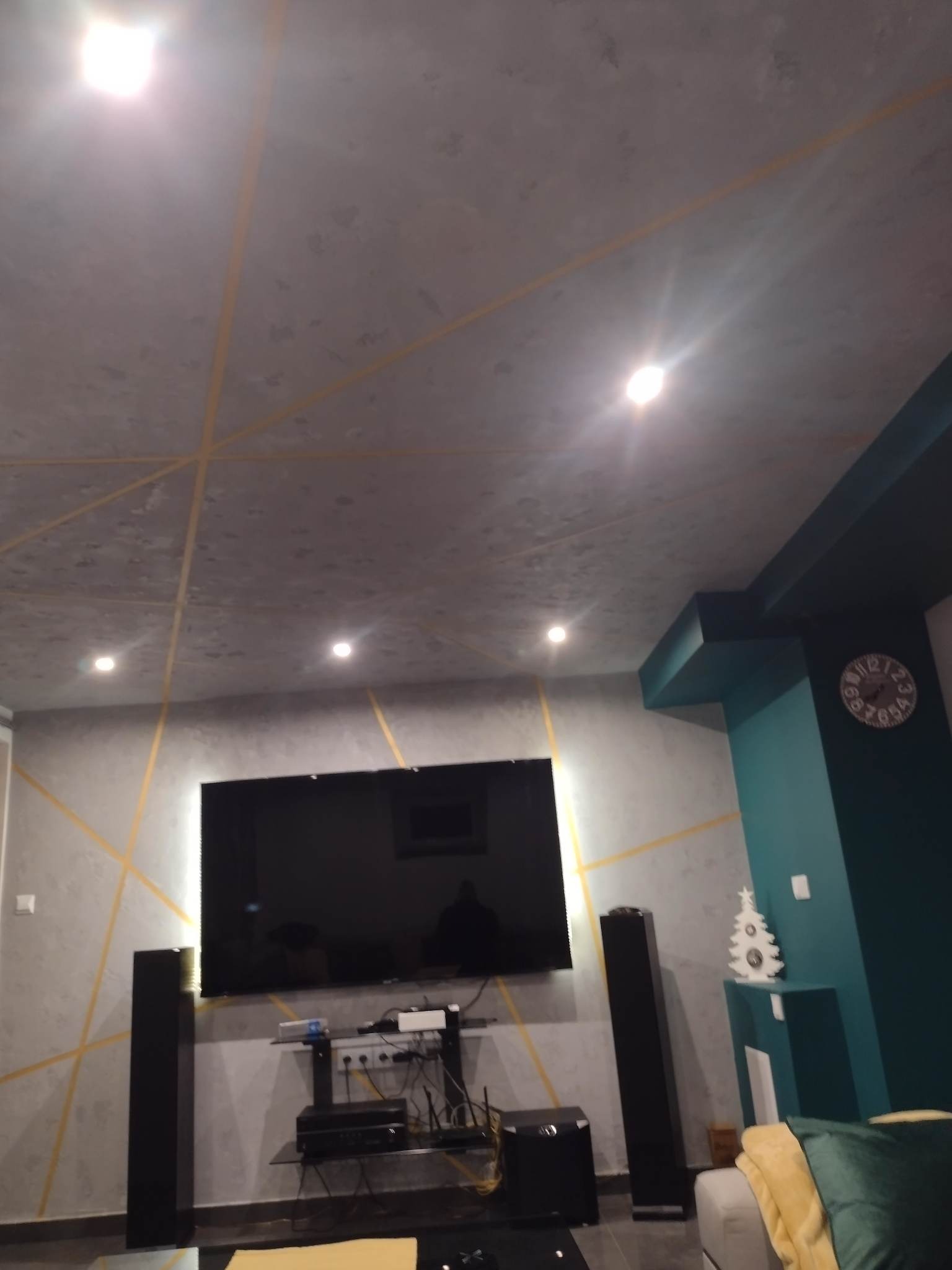 Szaro-turkusowe wnętrze salonu w Wieluniu z dekoracyjnymi złotymi liniami na ścianach i suficie, widoczny telewizor, głośniki i dekoracja świąteczna.