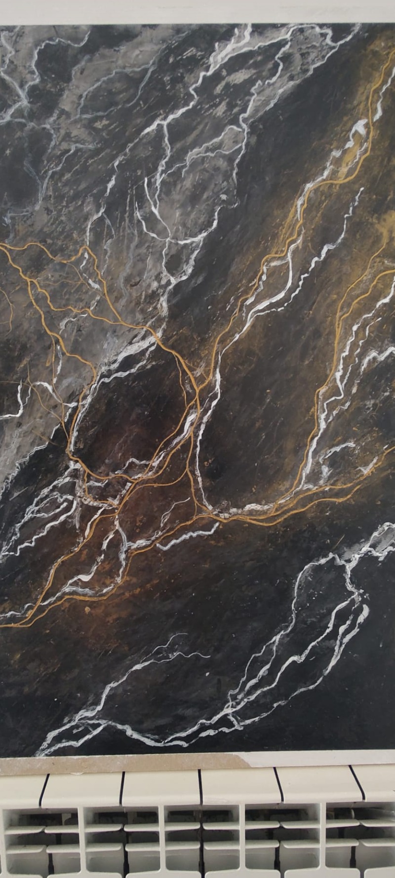 Czarno-szara ściana z efektem marmuru, podkreślona białymi i złotymi żyłkami, widoczny fragment grzejnika u dołu.