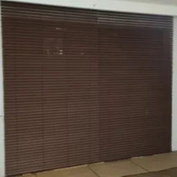 Ciemnobrązowe poziome osłony okienne zamontowane wewnątrz pomieszczenia z białymi ścianami i grzejnikiem, na podłodze rozłożone kartony ochronne.