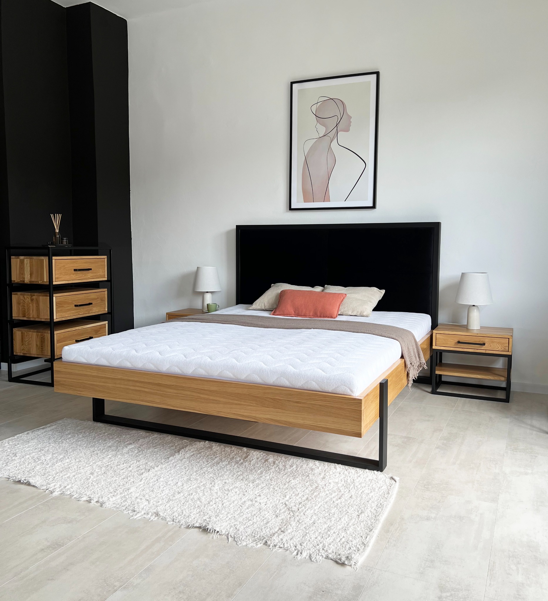 Nowoczesna sypialnia z dębowym łóżkiem na czarnych metalowych nogach, czarnym zagłówkiem, dębową szafką nocną i komodą z czarnymi elementami, na podłodze biały dywan shaggy.