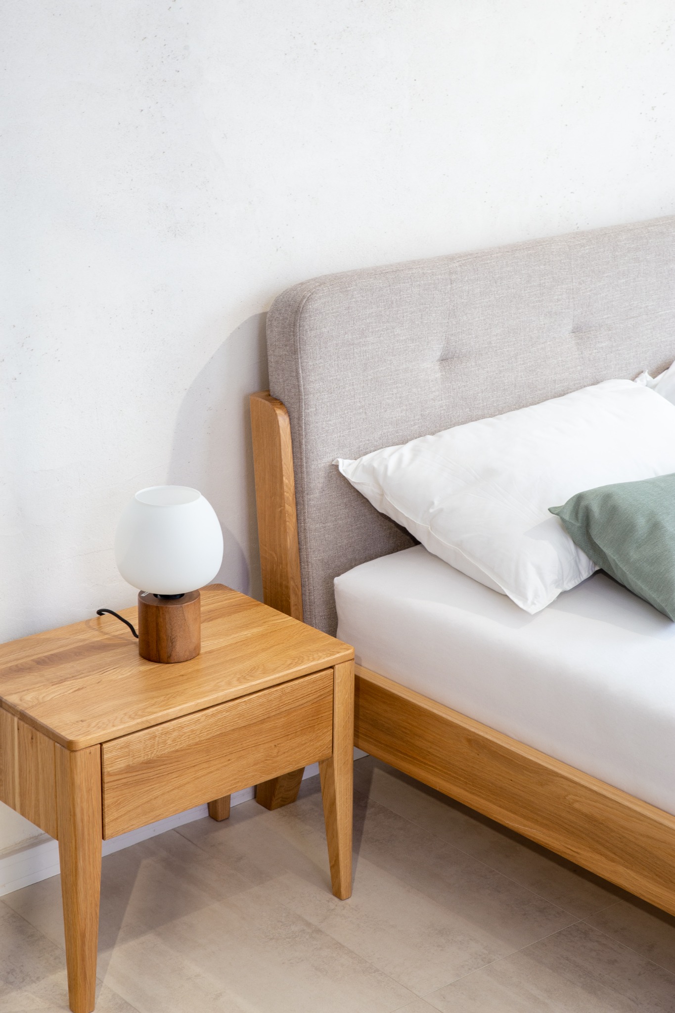 Drewniane łóżko z tapicerowanym zagłówkiem i szafka nocna z lampką w skandynawskim stylu, jasne wnętrze sypialni.