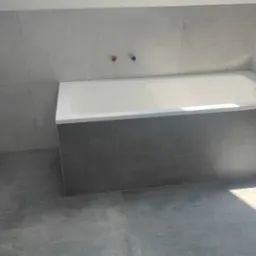 Nowoczesna łazienka z szarymi, matowymi płytkami na ścianach i podłodze, biała wanna z obudową z płytek, minimalistyczna armatura.