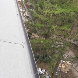 Usługi Dekarskie - Szara papa na dachu z zamontowaną rynną, widok z góry na drzewa i śmieci na ziemi.