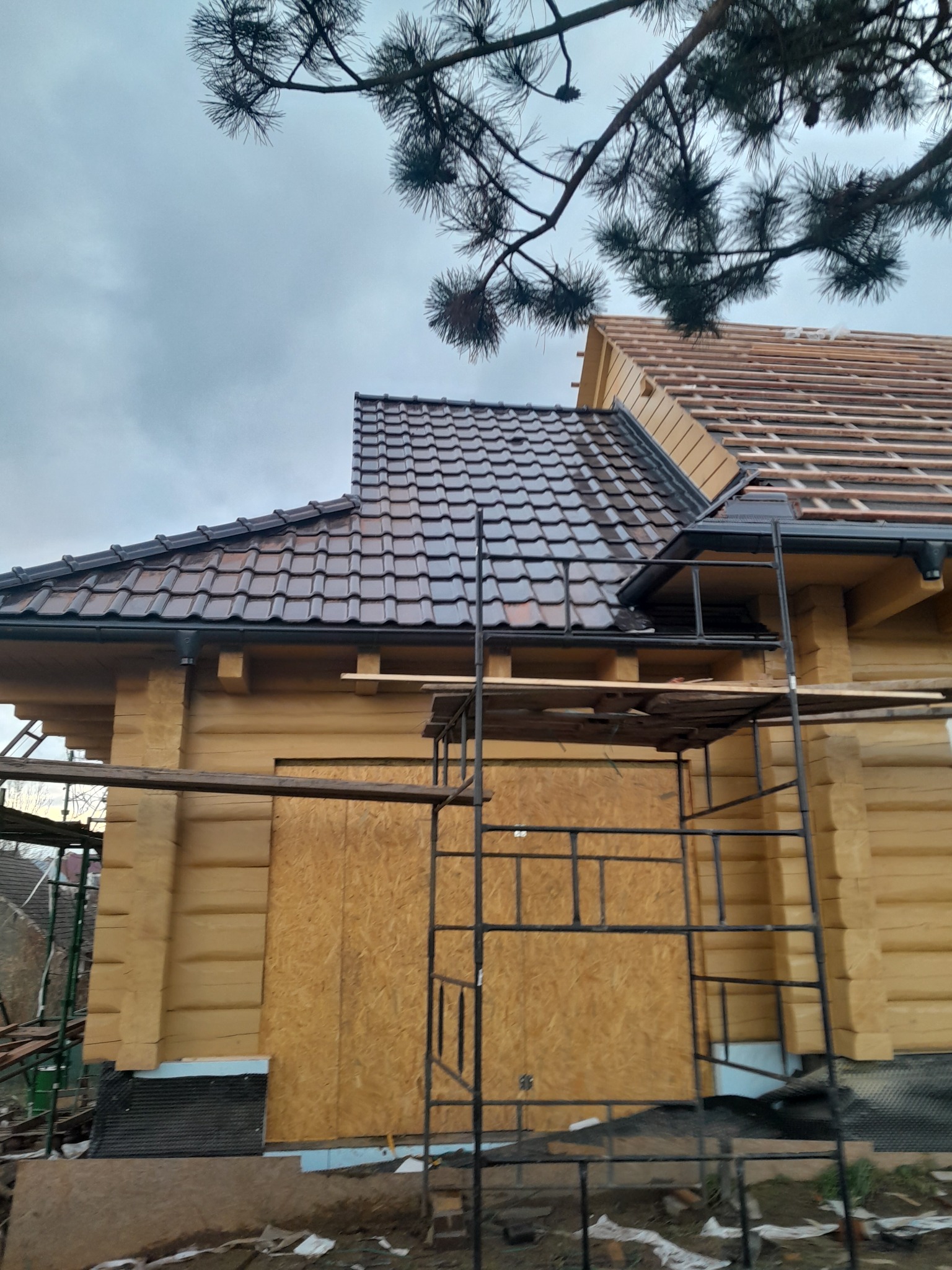 W trakcie budowy dachu z brązowej dachówki na drewnianym domu w Nysie, widoczne rusztowanie i fragment więźby dachowej.