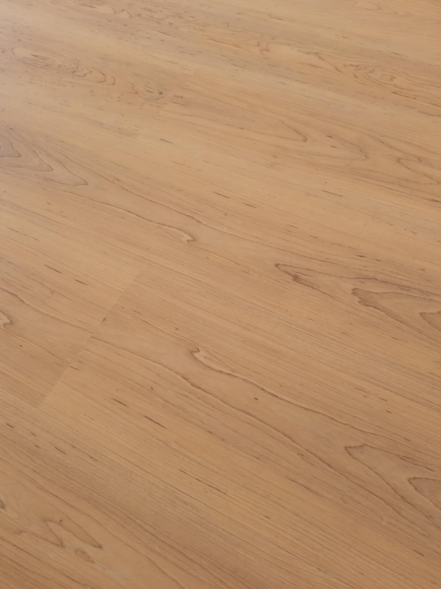 Jasne panele podłogowe z widocznym wzorem drewna, ułożone wzdłuż dłuższego boku pomieszczenia, z delikatnym połyskiem i widocznymi łączeniami.