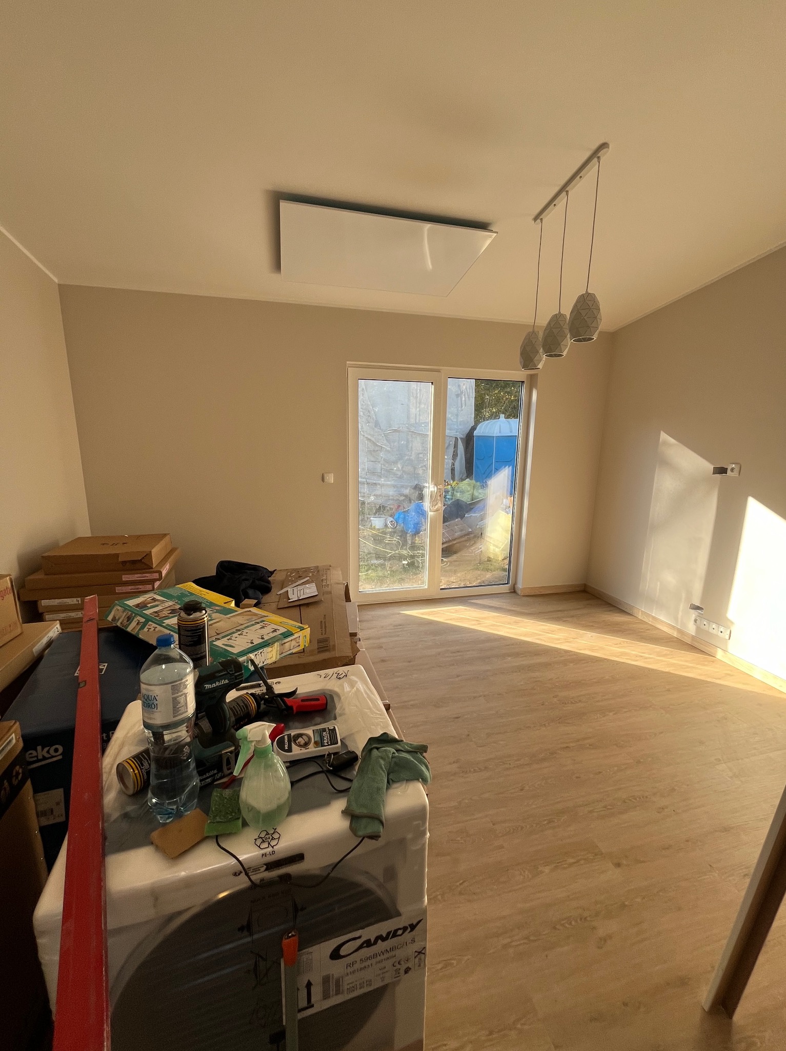 Pokój w trakcie remontu z ułożonymi jasnymi panelami podłogowymi, widoczne narzędzia i materiały budowlane, w tle przesuwne drzwi balkonowe.