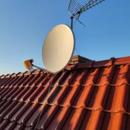 Antena satelitarna i antena naziemna zamontowane na dachu z czerwonej dachówki w słoneczny dzień.