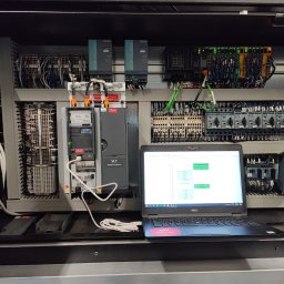 OMIautomatyka - Otwarta szafa sterownicza z widocznymi modułami, okablowaniem i laptopem Dell z uruchomionym oprogramowaniem diagnostycznym, podłączonym do szafy kablem USB.