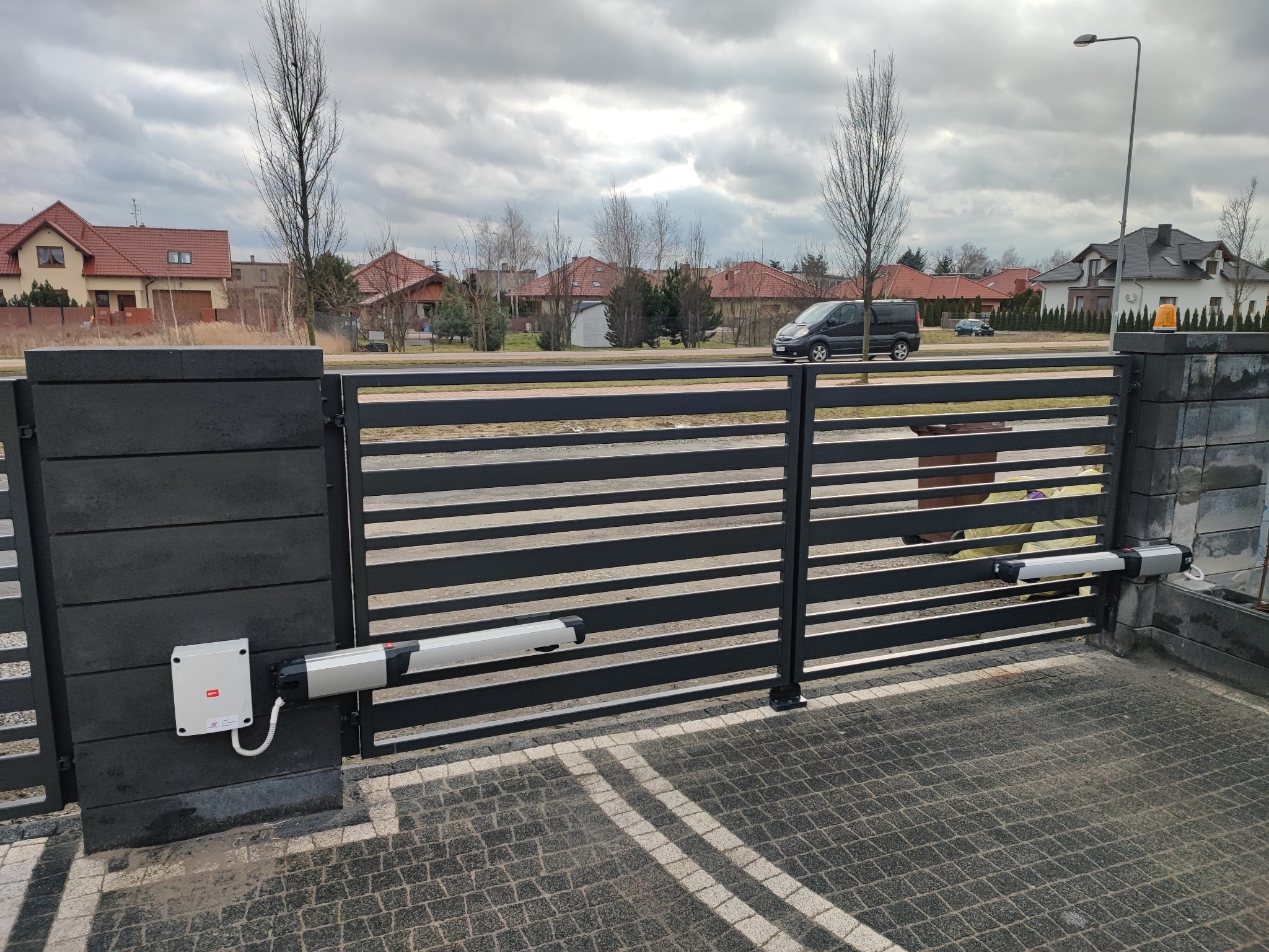Czarna, pozioma brama wjazdowa z zainstalowaną automatyką na posesji w Gębicach, widok na ulicę i zabudowania w tle.