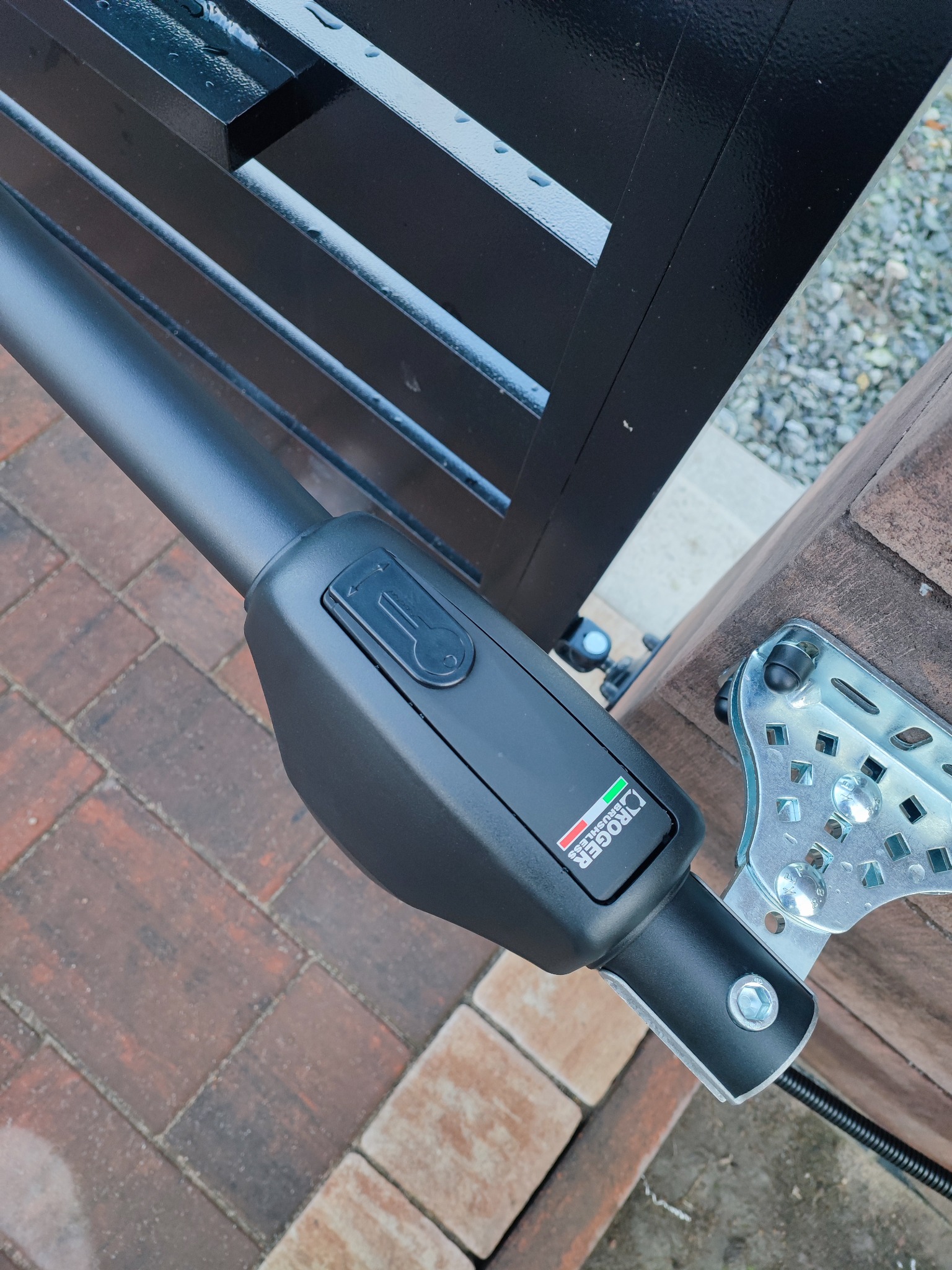 Czarny siłownik bramy marki Roger przymocowany do słupka, widoczne logo producenta i fragment czarnej bramy.