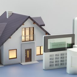 Dawid Cyganik - System alarmowy z centralą, czujnikami ruchu i syreną alarmową, prezentowany na tle modelu domu jednorodzinnego w Krakowie. Na ekranie centrali widoczny status 'rozbrojony'.