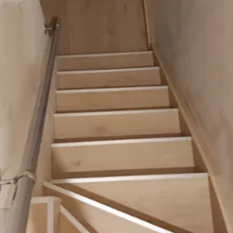 Schody wewnętrzne wykończone panelami drewnopodobnymi z białą listwą, widok z góry, fragment metalowej poręczy po lewej stronie.