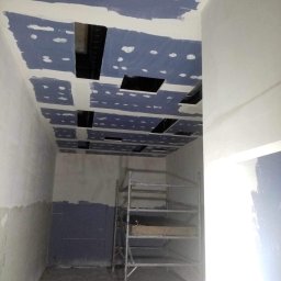 ROBERT MYKYTA RMD - Montaż płyt gipsowo-kartonowych na suficie z widocznymi otworami na instalacje, ściany przygotowane do dalszych prac wykończeniowych, widoczne rusztowanie.