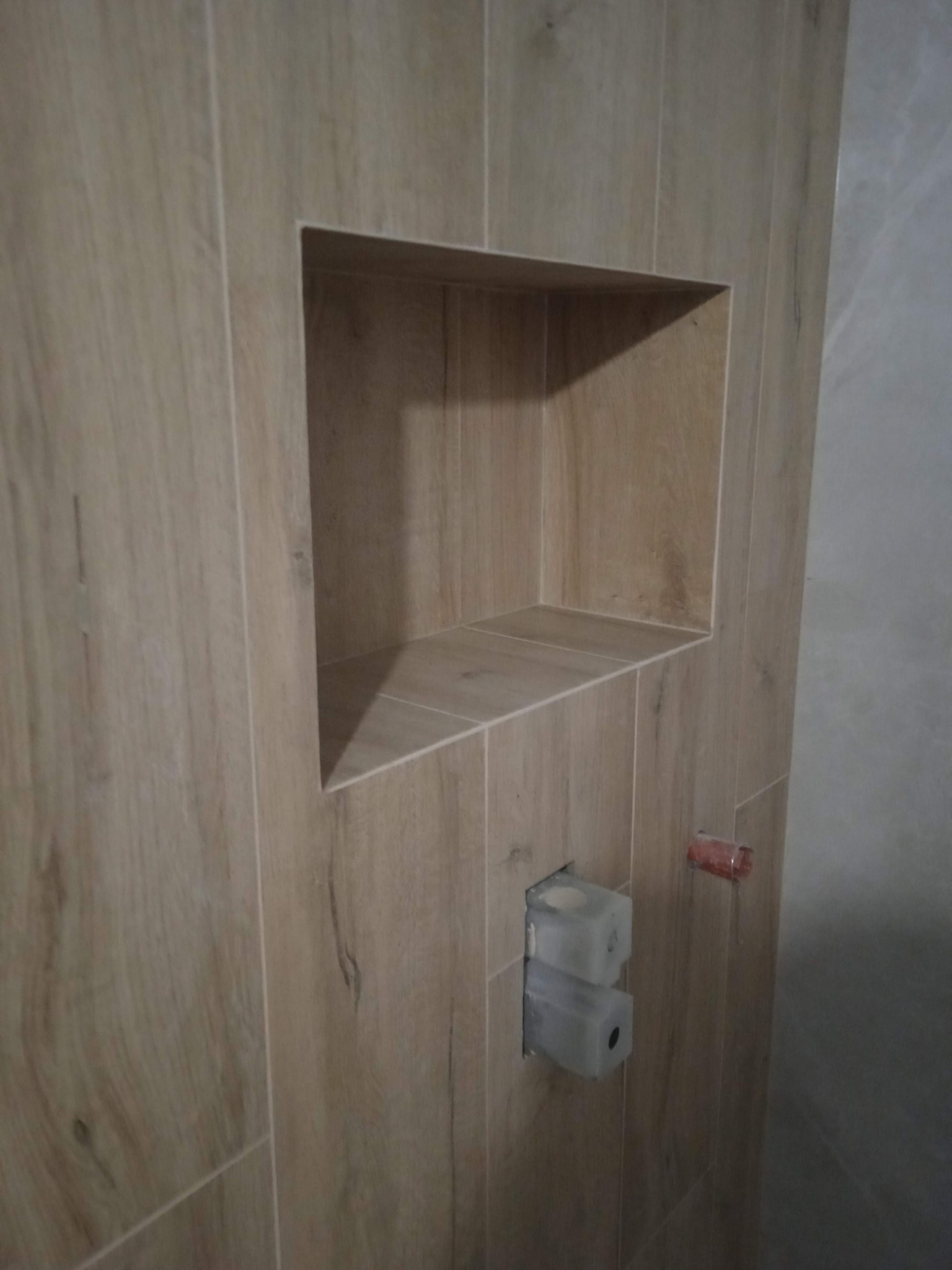 Wnęka wyłożona płytkami imitującymi drewno w łazience, z widocznymi elementami instalacji wodnej w ścianie.