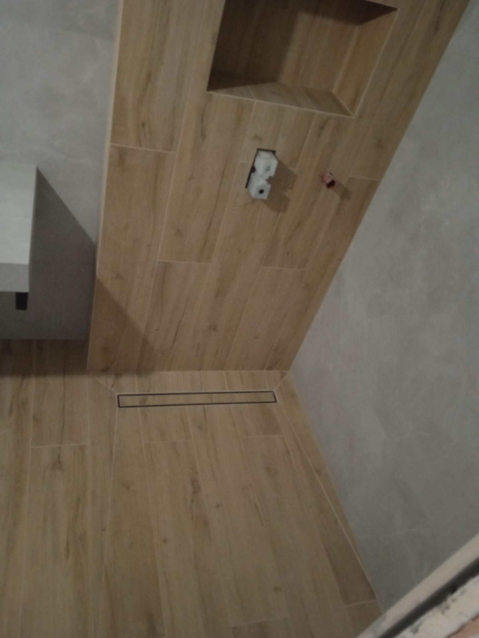 Ukończona łazienka z drewnopodobnymi płytkami ceramicznymi na ścianach i podłodze, z odpływem liniowym w strefie prysznicowej oraz wnęką w ścianie.