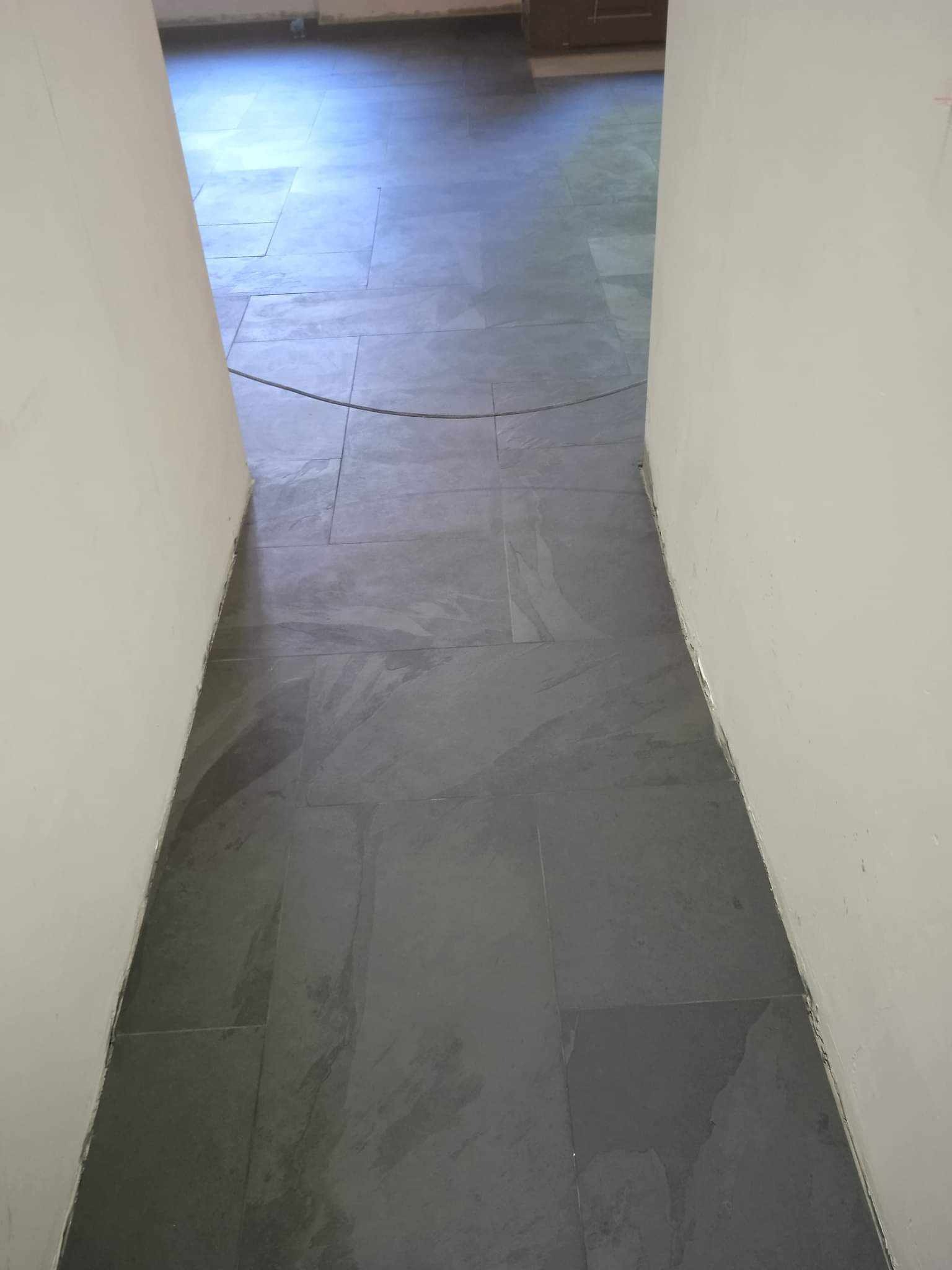 Ułożona szara, matowa podłoga z płytek pomiędzy dwiema białymi ścianami, widoczny przewód elektryczny na posadzce.