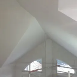 Poddasze z oknami w kształcie łuków, świeżo po pracach wykończeniowych, widoczne rusztowanie i kabel zwisający z sufitu.