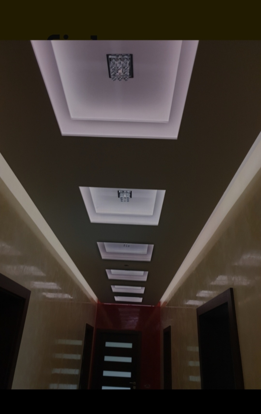 Długi korytarz z ciemnymi drzwiami i dekoracyjnym sufitem z wnękami i oświetleniem punktowym oraz żyrandolem w pierwszej wnęce.