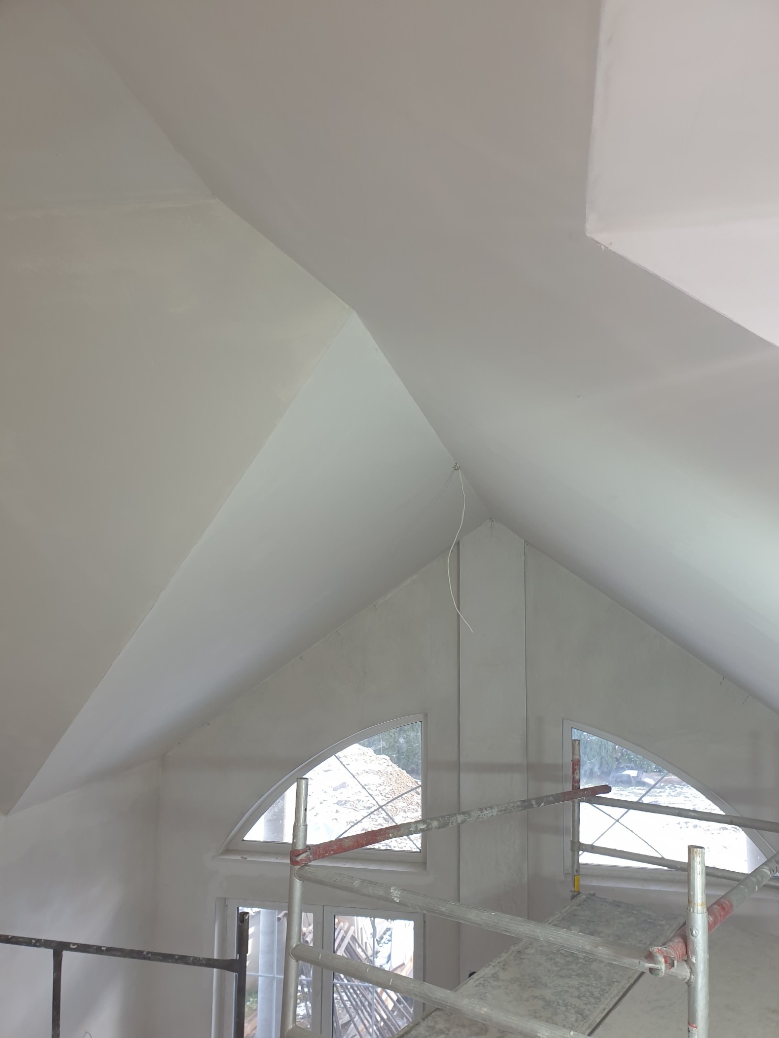 Poddasze z oknami w kształcie łuków, świeżo po pracach wykończeniowych, widoczne rusztowanie i kabel zwisający z sufitu.