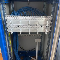 Electro4you - Panel krosowniczy w szafie rack z uporządkowanymi kablami Ethernet w kolorze niebieskim. Widoczne oznaczenia portów i moduły zasilające.