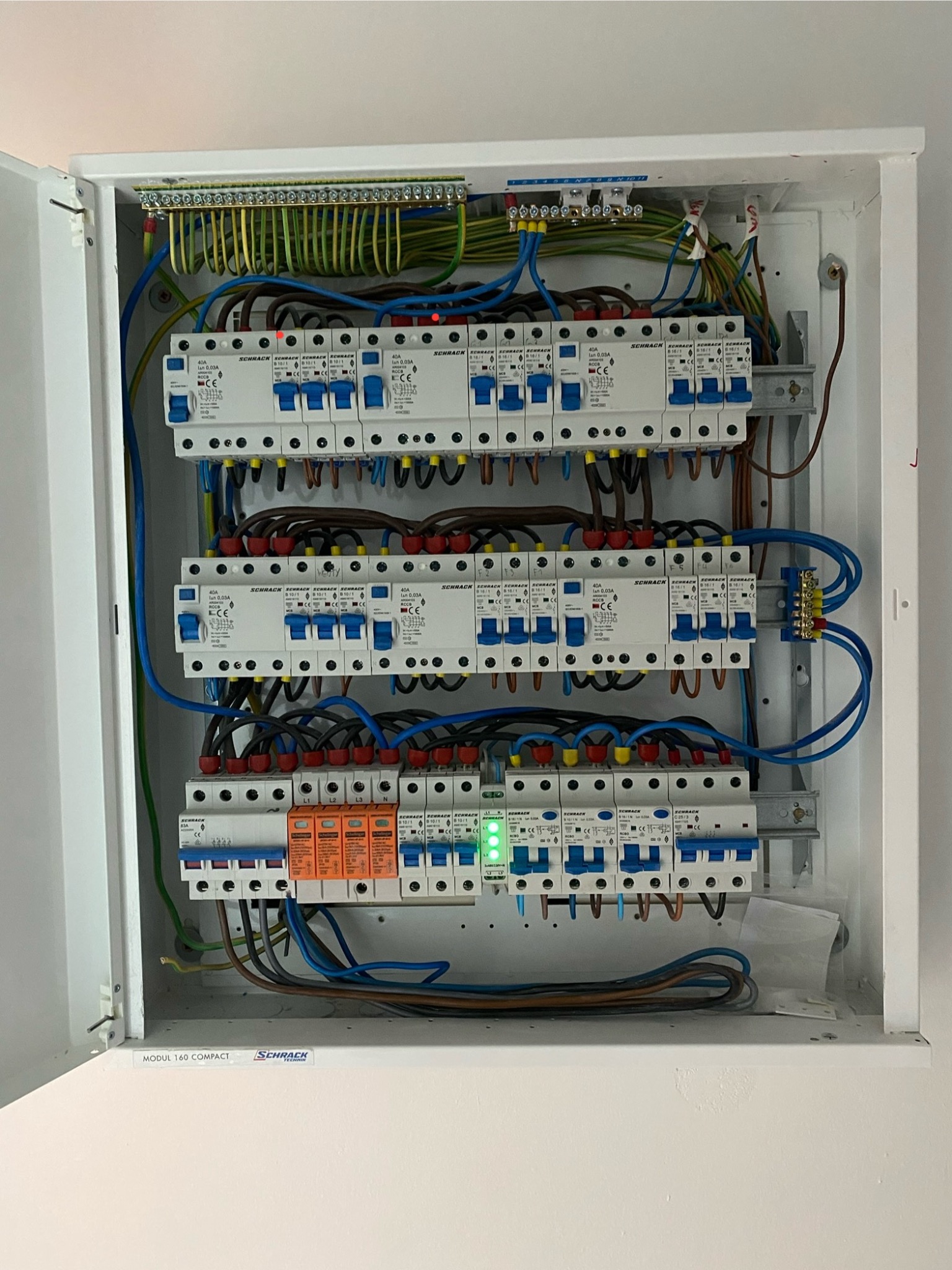 Rozdzielnica elektryczna Schrack w białej obudowie, z widocznymi bezpiecznikami, przewodami i listwami zaciskowymi. Instalacja po montażu, widok z bliska.