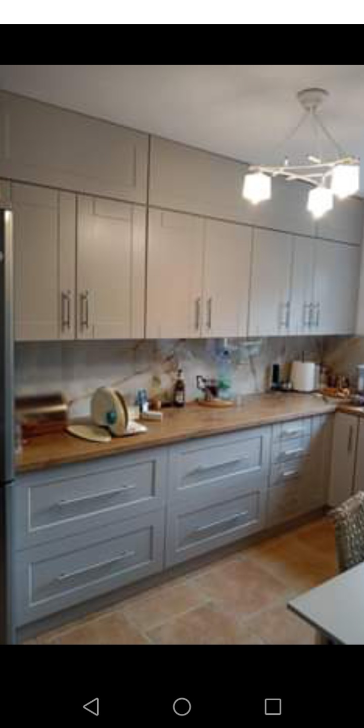 Szara zabudowa kuchenna z drewnianym blatem, widoczne naczynia na blacie i nowoczesna lampa sufitowa.