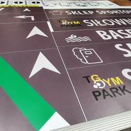 Sebastian Matusik Firma Handlowo-Usługowa - Brązowe tablice informacyjne z białymi napisami i piktogramami, wskazujące kierunek do sklepu sportowego, siłowni, basenów i sauny, z logo TGym Park.