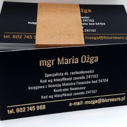 Sebastian Matusik Firma Handlowo-Usługowa - Stos wizytówek z czarnym tłem i złotym tekstem, owinięty brązowym papierem, prezentujący dane kontaktowe mgr Marii Ożgi, specjalisty ds. rachunkowości z Bytomia.