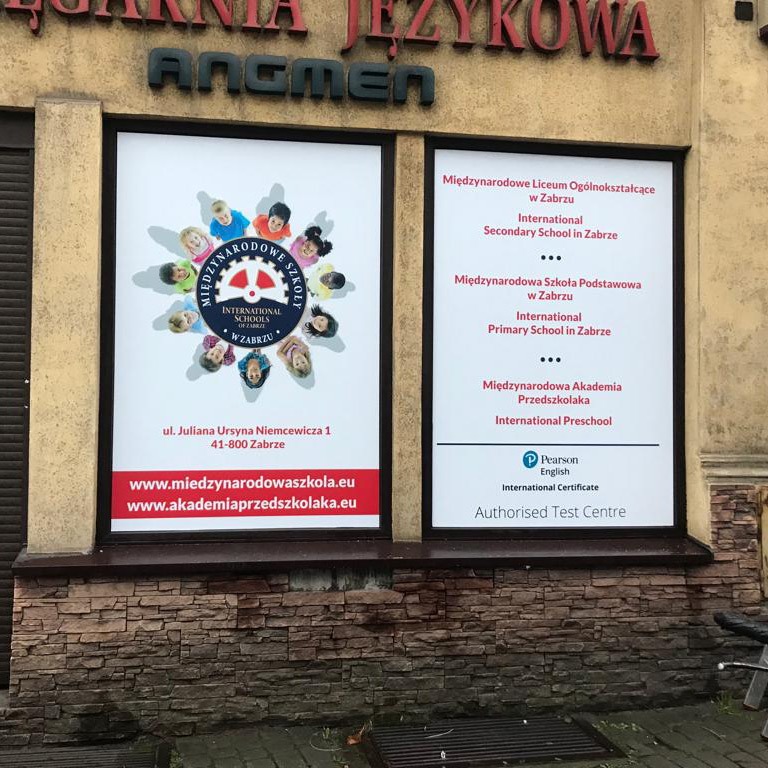 Oklejone witryny językowej szkoły z informacjami o placówkach edukacyjnych: liceum, szkoła podstawowa, przedszkole, oraz logo międzynarodowej szkoły z dziećmi wokół koła i adresami stron...